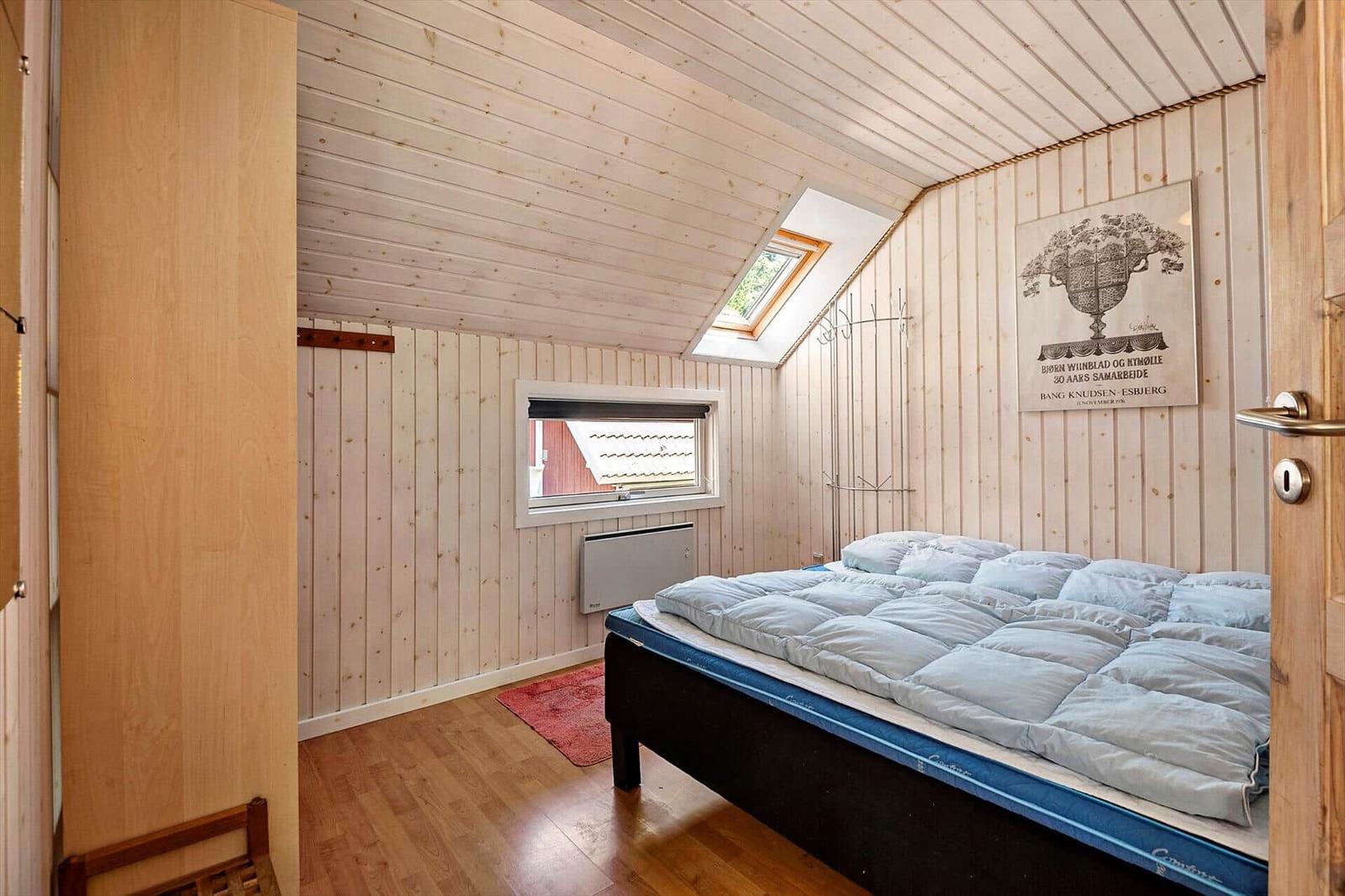 Schlafzimmer mit Holzwand, Dachfenster und Bett mit blauer Matratze.
