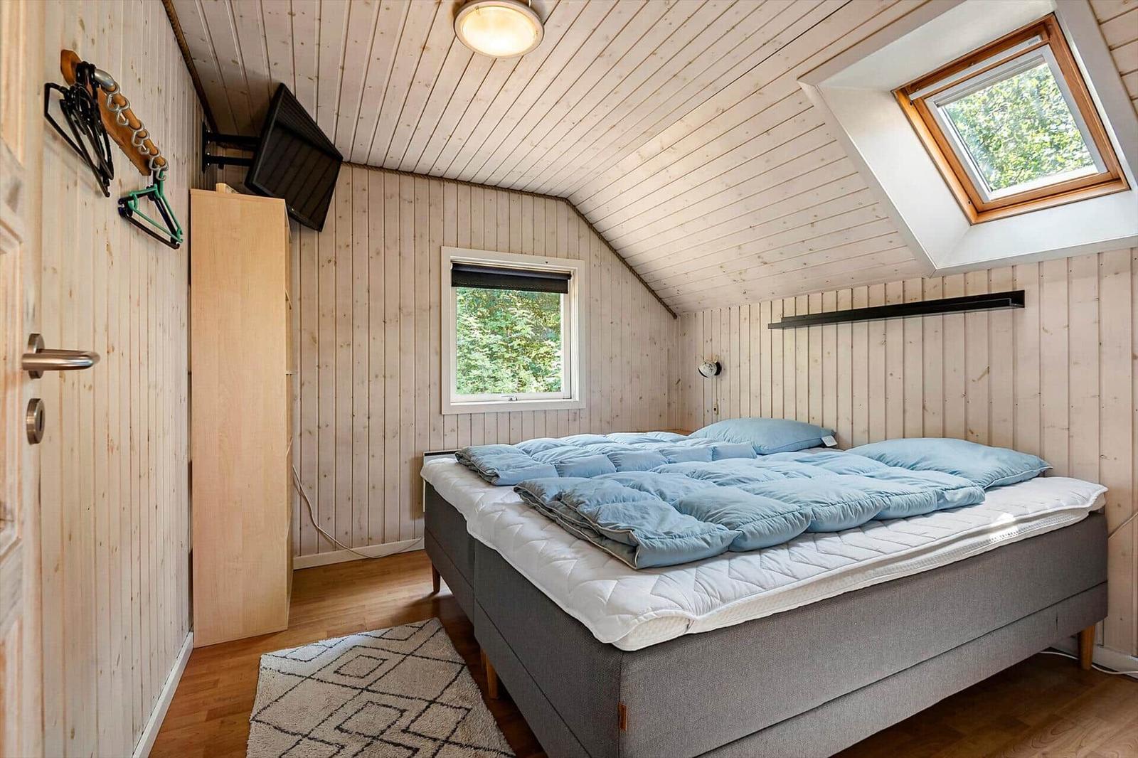 Schlafzimmer mit Dachfenster, Bett und Kleiderständer an der Wand.