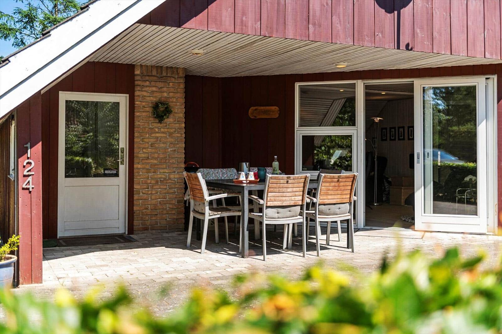 Außenbereich mit Tisch und Stühlen vor einem Haus mit rotem Holzverkleidung und Glasfront.