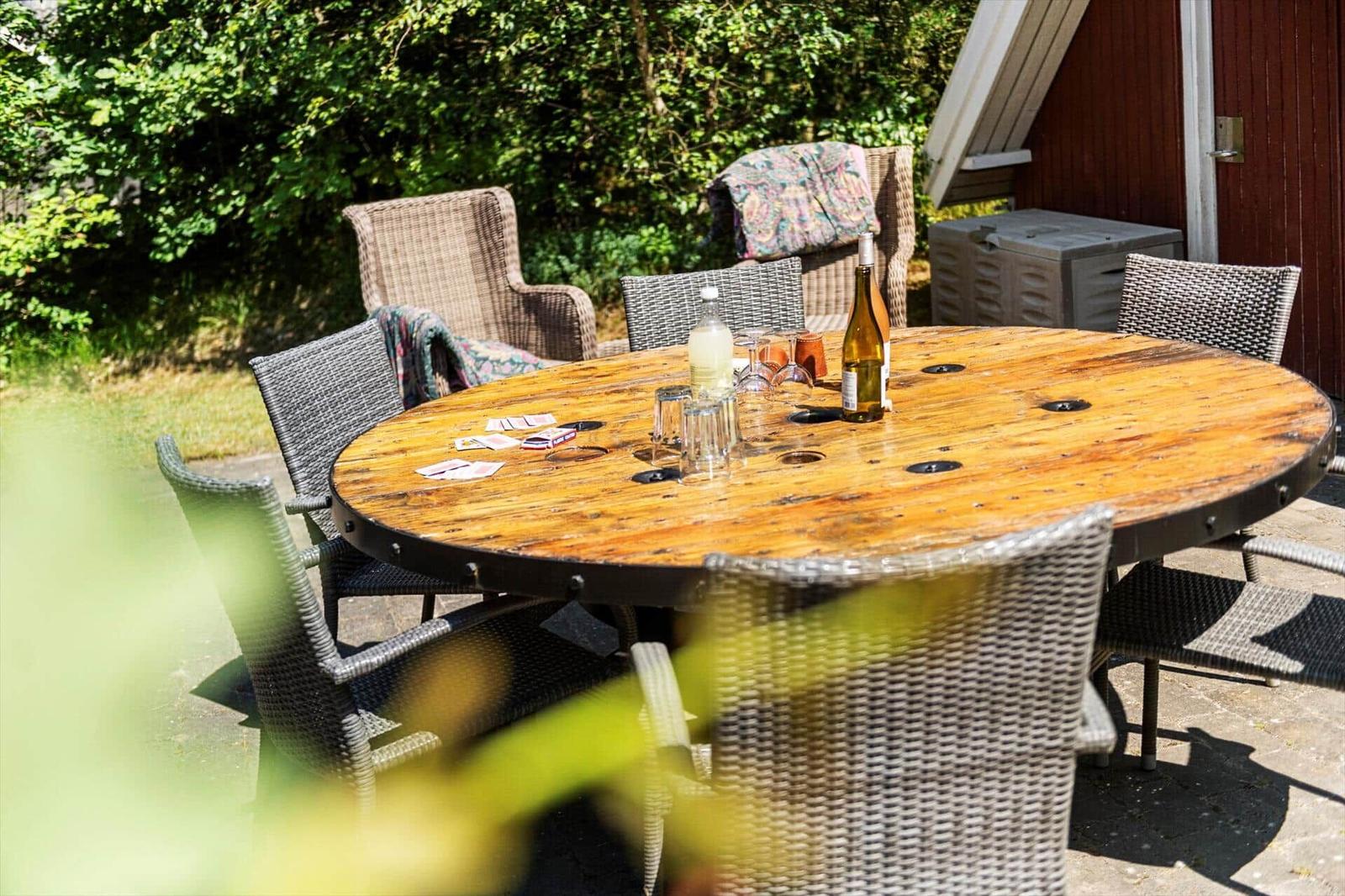 Runder Holztisch mit Stühlen im Garten. Auf dem Tisch stehen Gläser und eine Flasche.