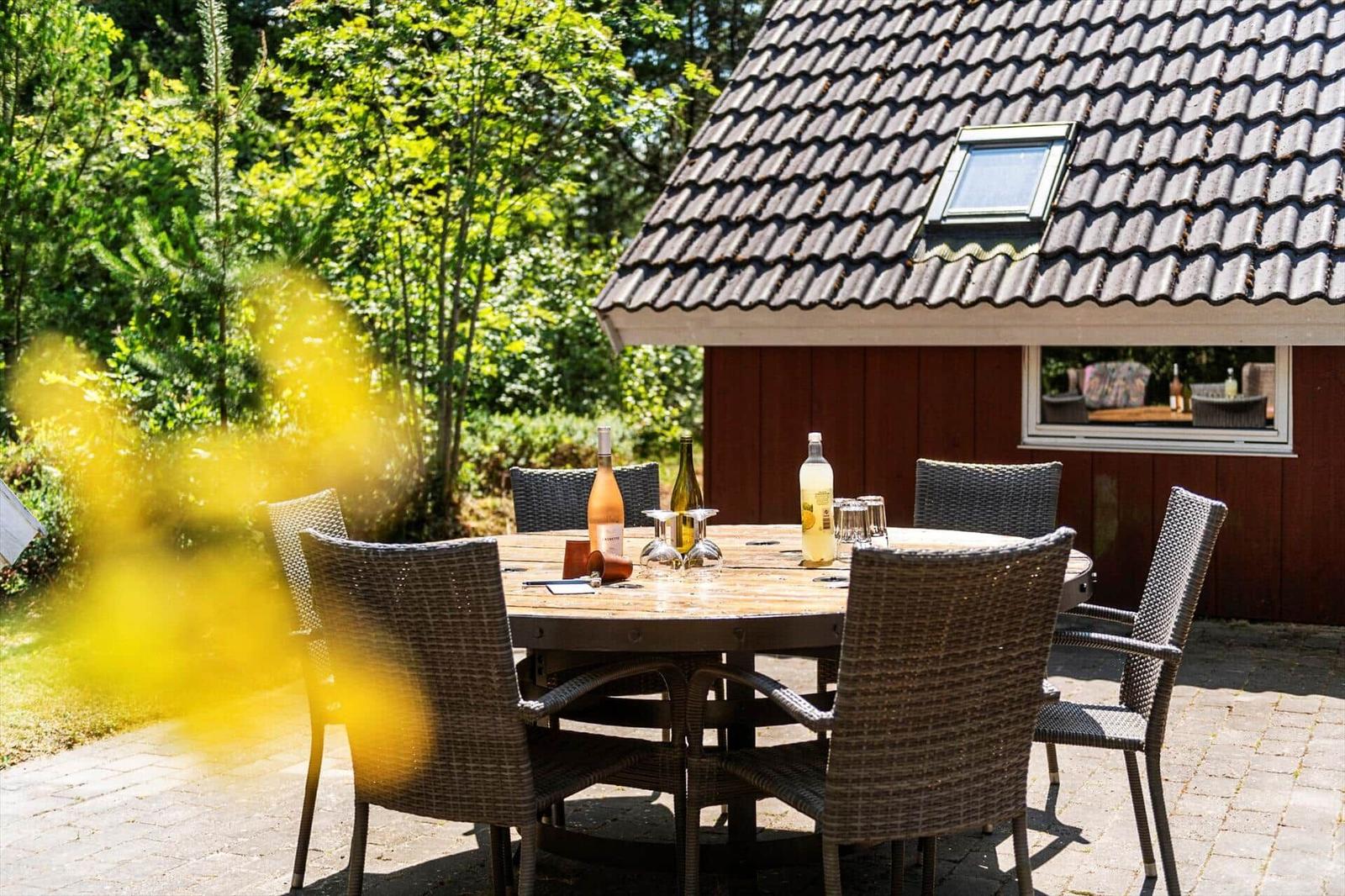 Runder Tisch mit Stühlen im Garten vor einem Haus mit Dachfenster.