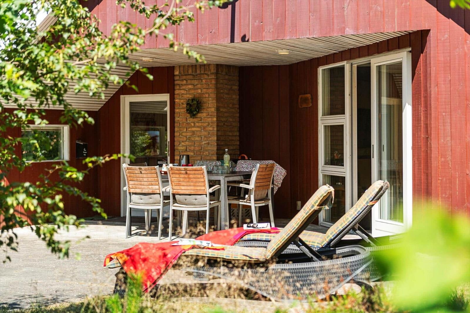 Roter Holzhaus mit Terrasse, Tisch, Stühlen und Liegen im Freien.