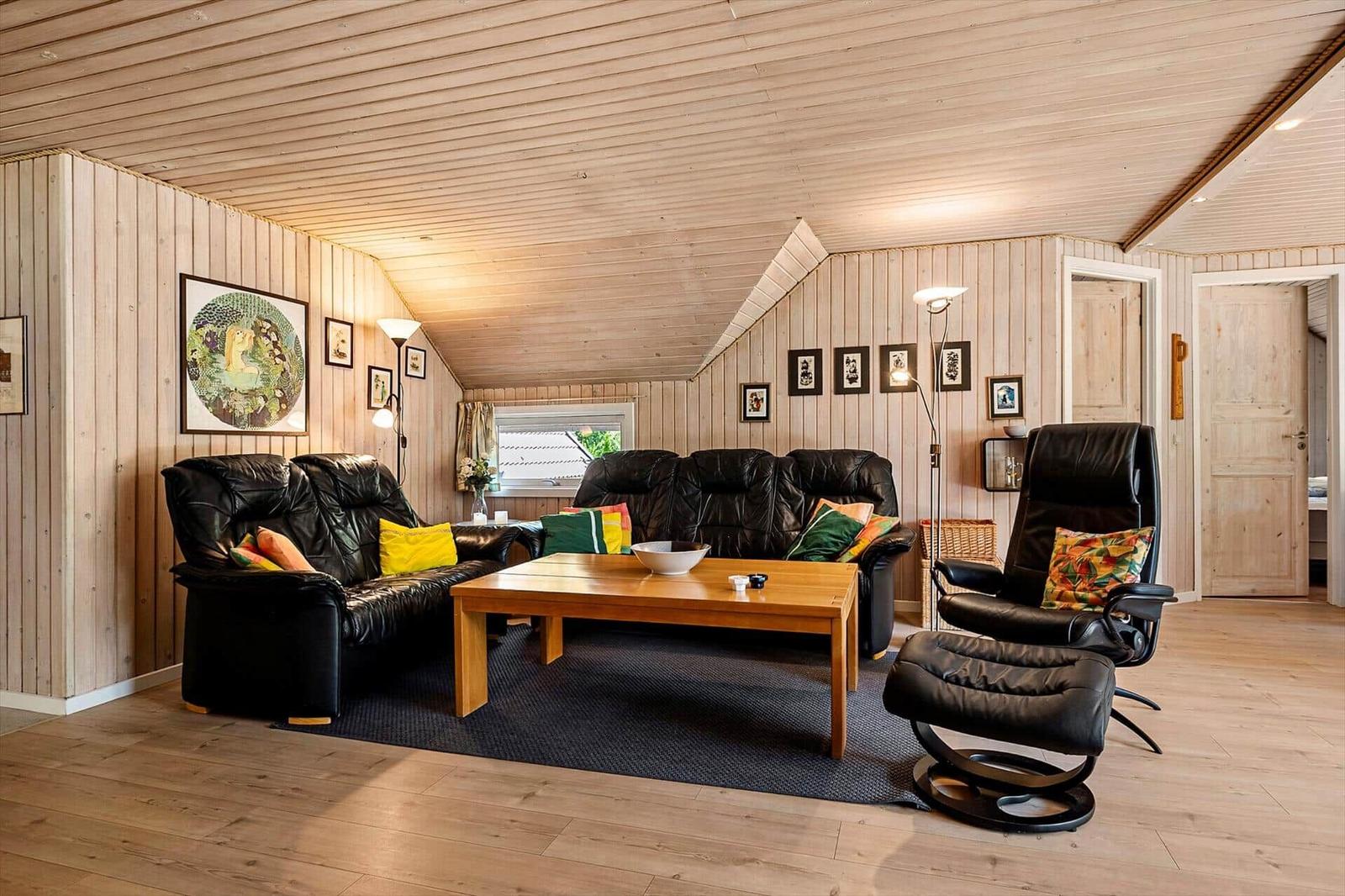 Wohnzimmer mit schwarzen Ledersofas, Holztisch und Holzwandverkleidung.