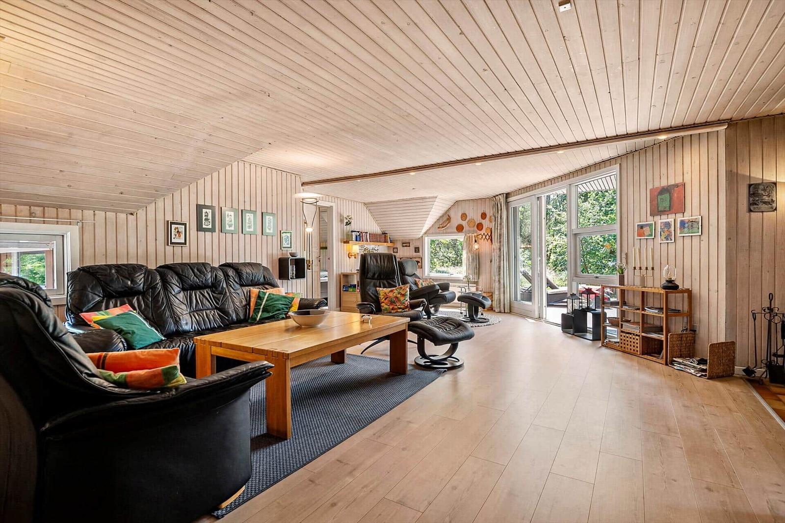 Wohnzimmer mit Holzdecke, Sofa, Sessel und Terrassentür