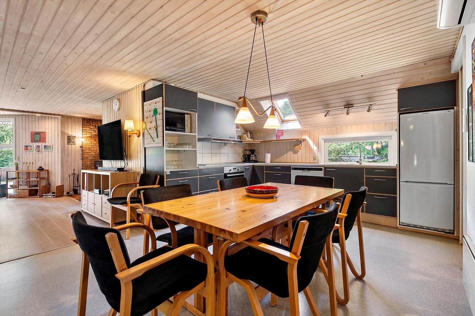 Küche mit Essbereich, Holztisch, schwarzen Stühlen und integriertem Kühlschrank.