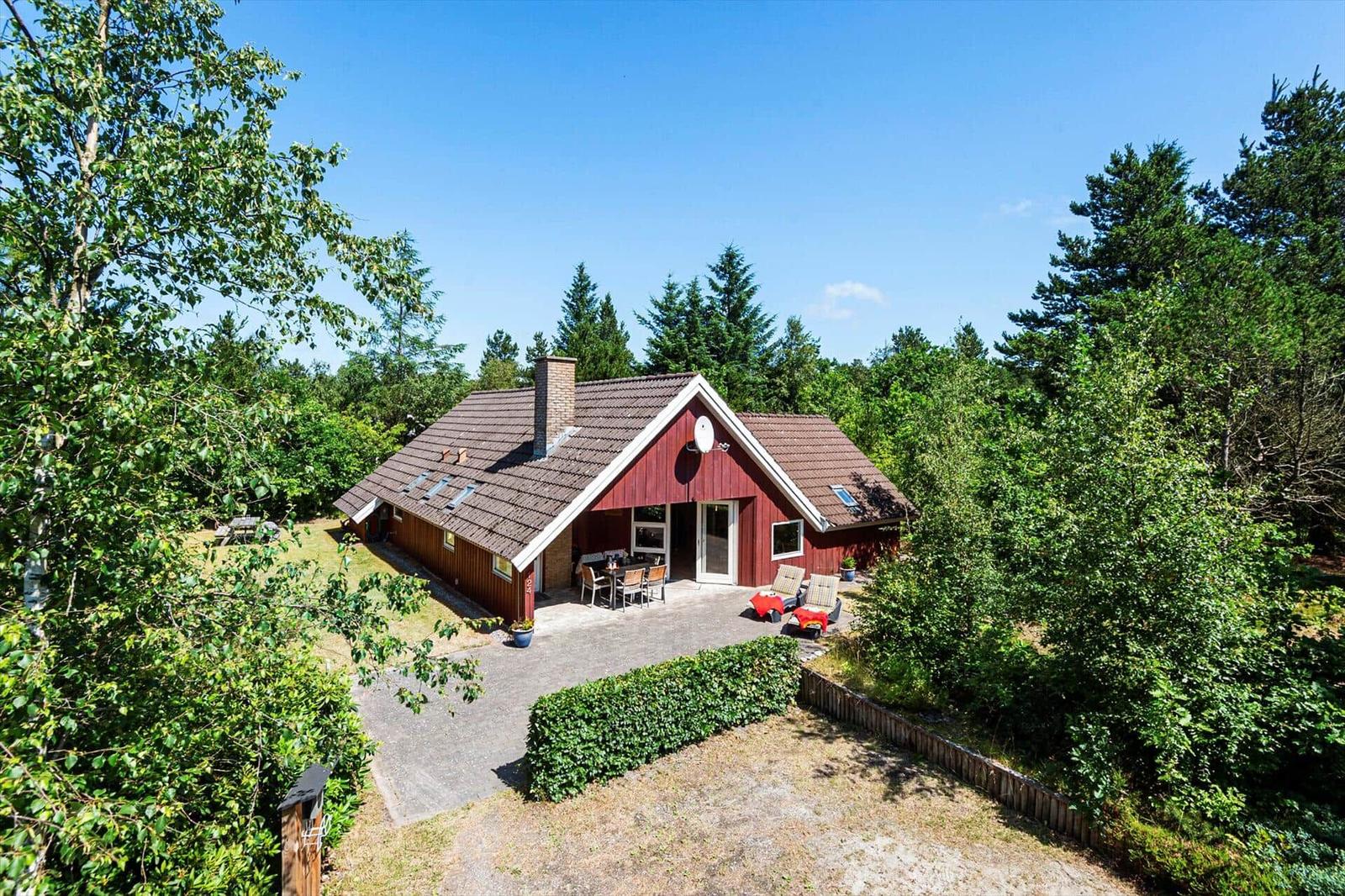 Rotes Holzhaus mit Terrasse und Garten in grüner Umgebung.