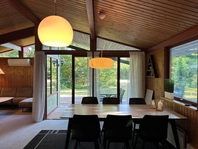Essbereich mit Tisch und Stühlen unter Holzdecke und großen Fenstern.