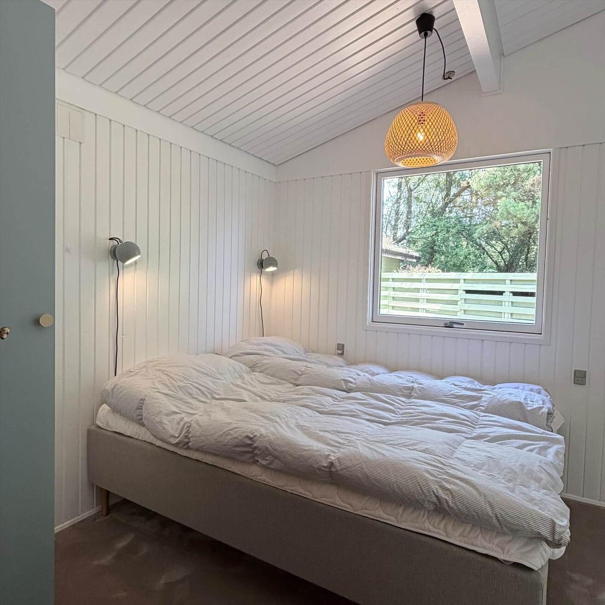 Schlafzimmer mit Doppelbett, Fenster und Deckenleuchte.