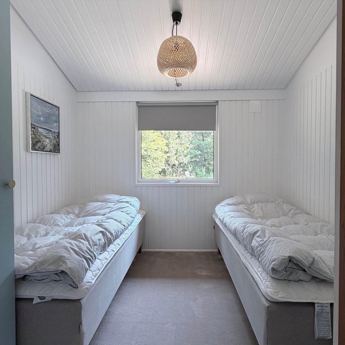 Zwei Schlafplätze mit Matratzen und Bettwäsche. Fenster mit Blick auf Bäume. Decke mit Pendelleuchte.