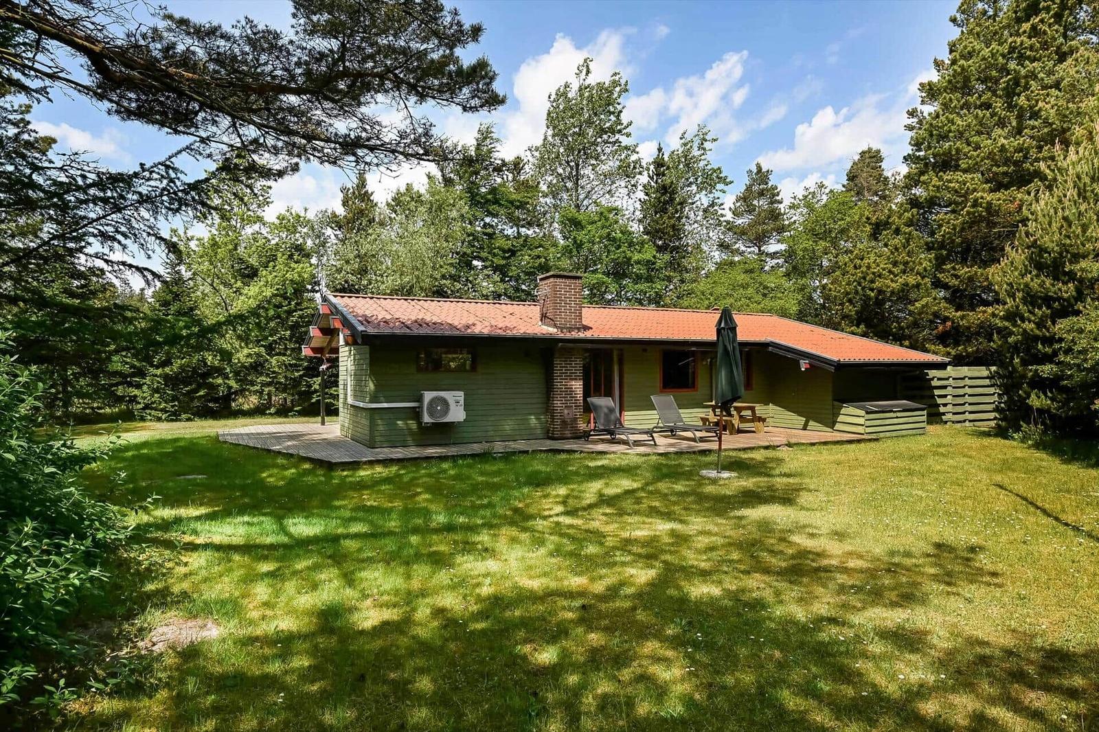 Ein grünes Haus mit Terrasse, Liegen und Grillplatz im Wald.