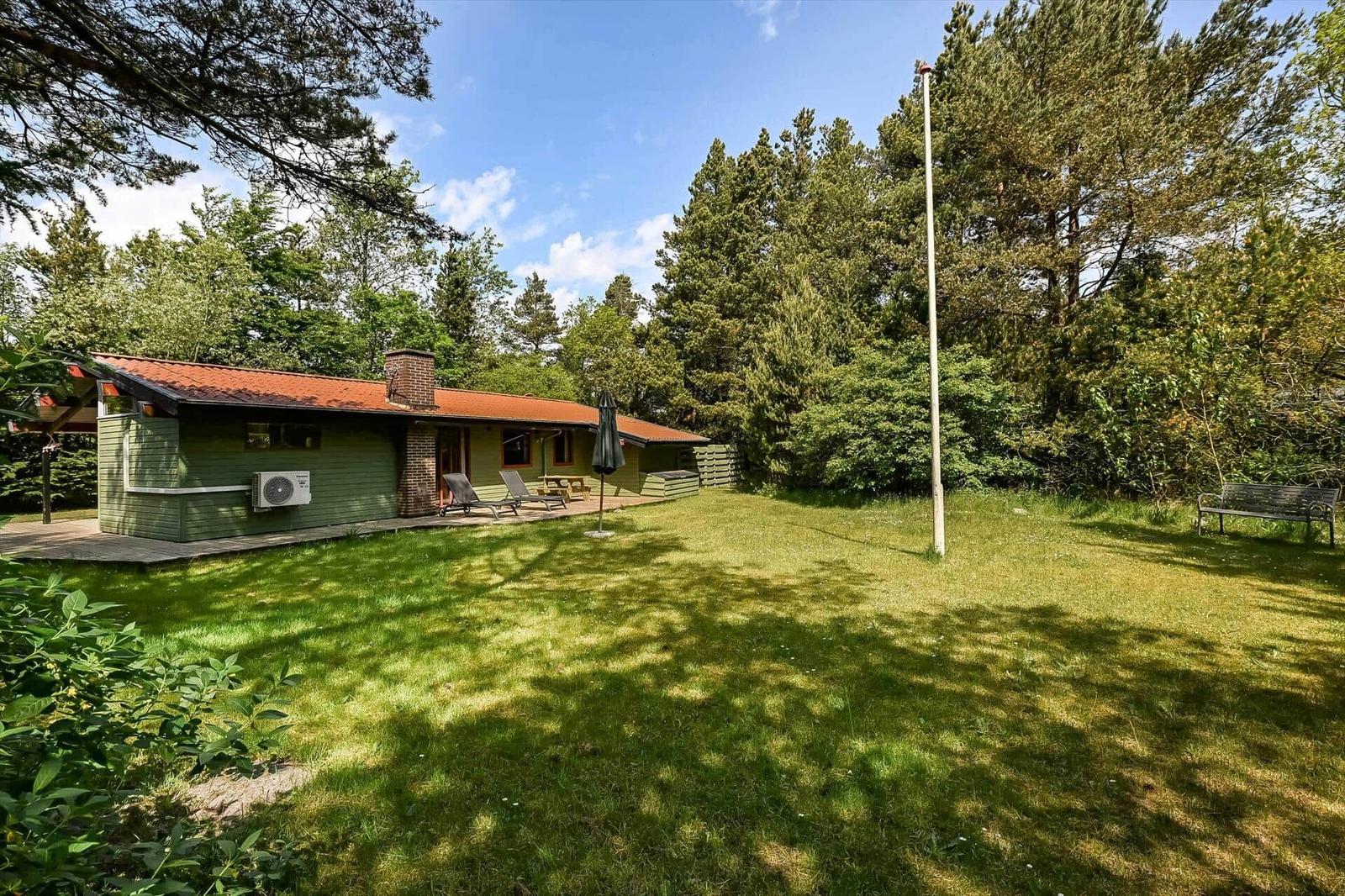 Ein grünes Haus mit Terrasse, Liegen und Grillplatz im Grünen.