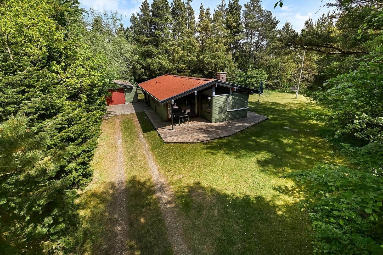 Grüne Hütte mit Holzterrasse im Wald. Garten und Grillplatz.