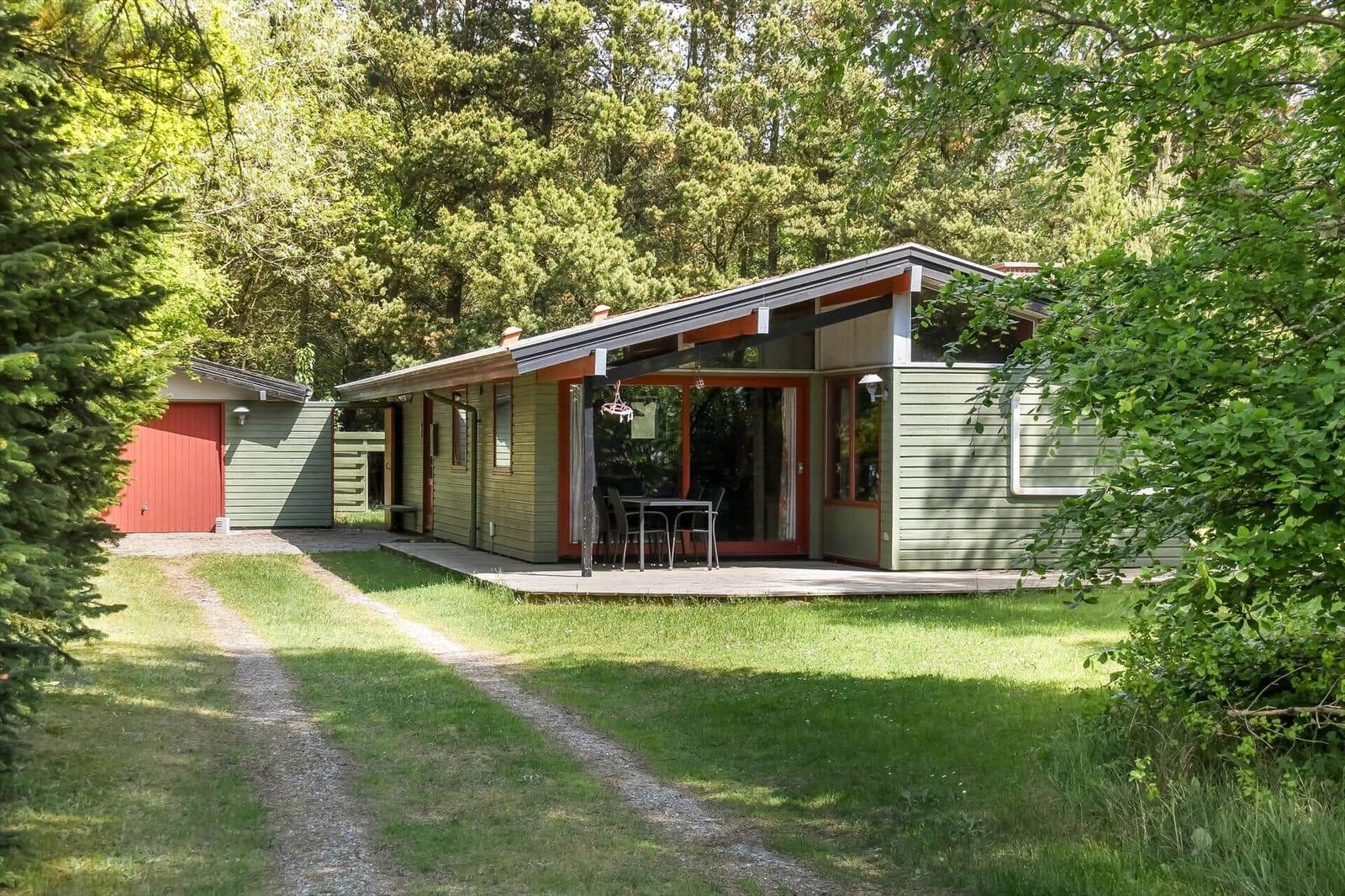 Grünes Ferienhaus mit Terrasse und Grillplatz im Wald. Holzverkleidung und rote Akzente.