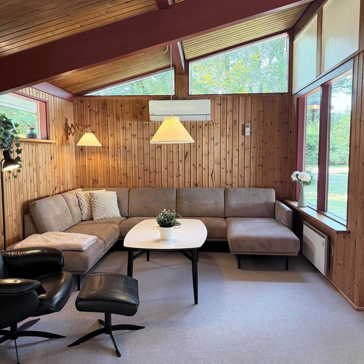 Wohnzimmer mit L-förmigem Sofa, Tisch und Fenstern. Holzwände und Decke.