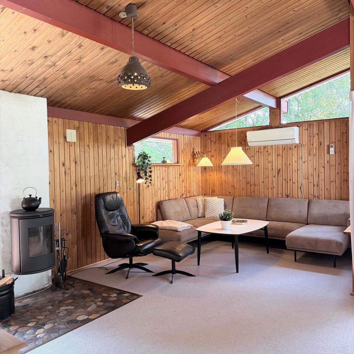 Wohnzimmer mit Sofa, Sessel, Kamin und Holzwandverkleidung.