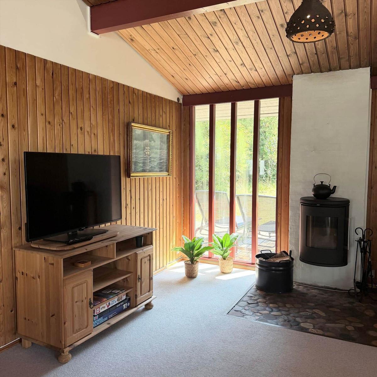Wohnzimmer mit Holzwand, Fernseher, Kaminofen und Glastür zum Garten.
