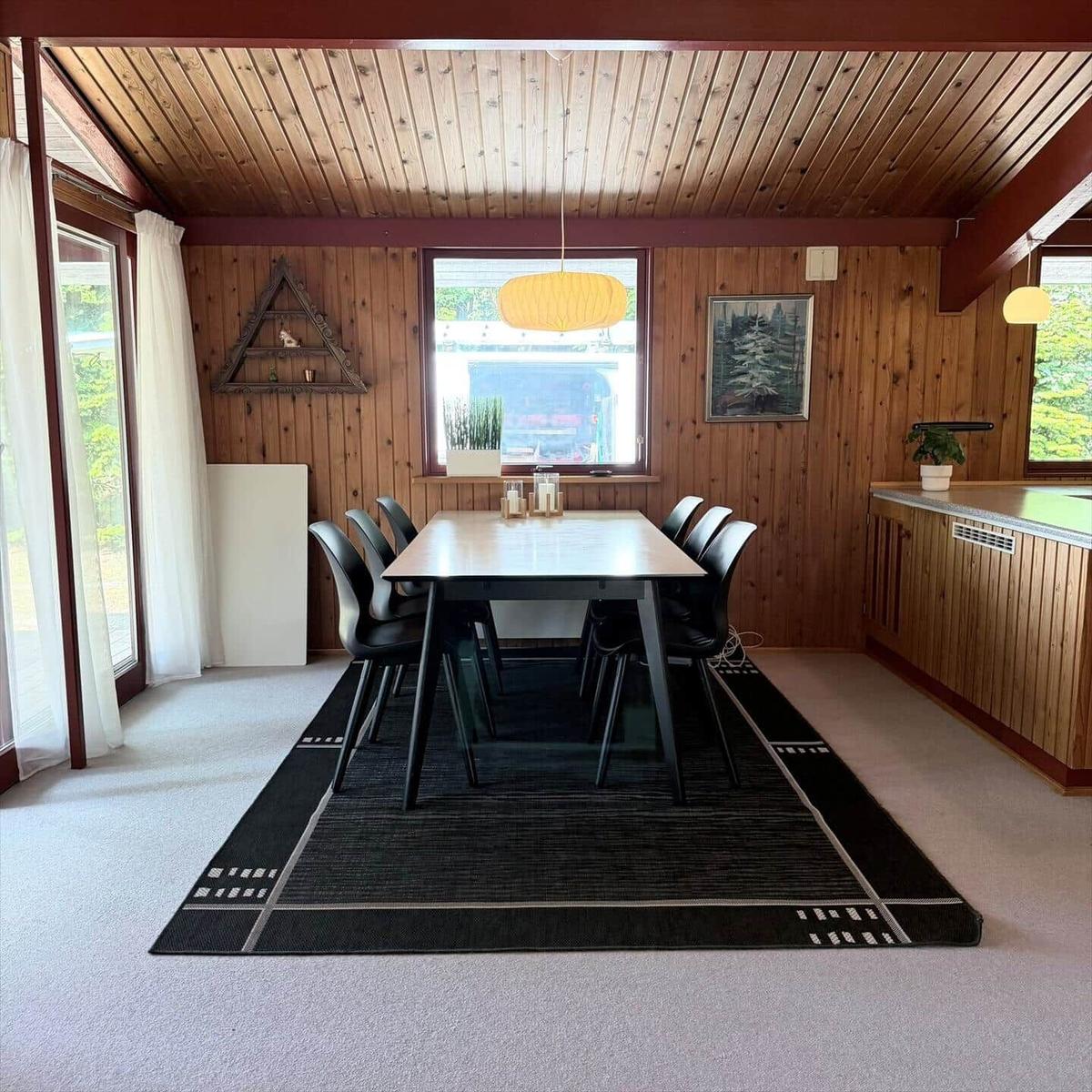 Esszimmer mit Holzwand, Tisch, Stühlen und Fenster.