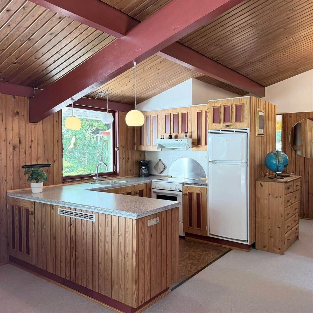 Küche mit Holzelementen, Kühlschrank, Herd und Fenster zur Außenseite.