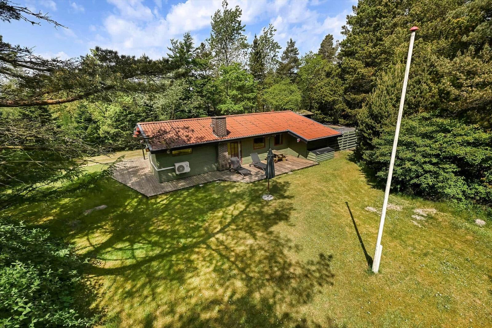 Grünes Haus mit Terrasse, Liegen und Grillplatz im Wald. Roter Dachfirst und Holzdecke.