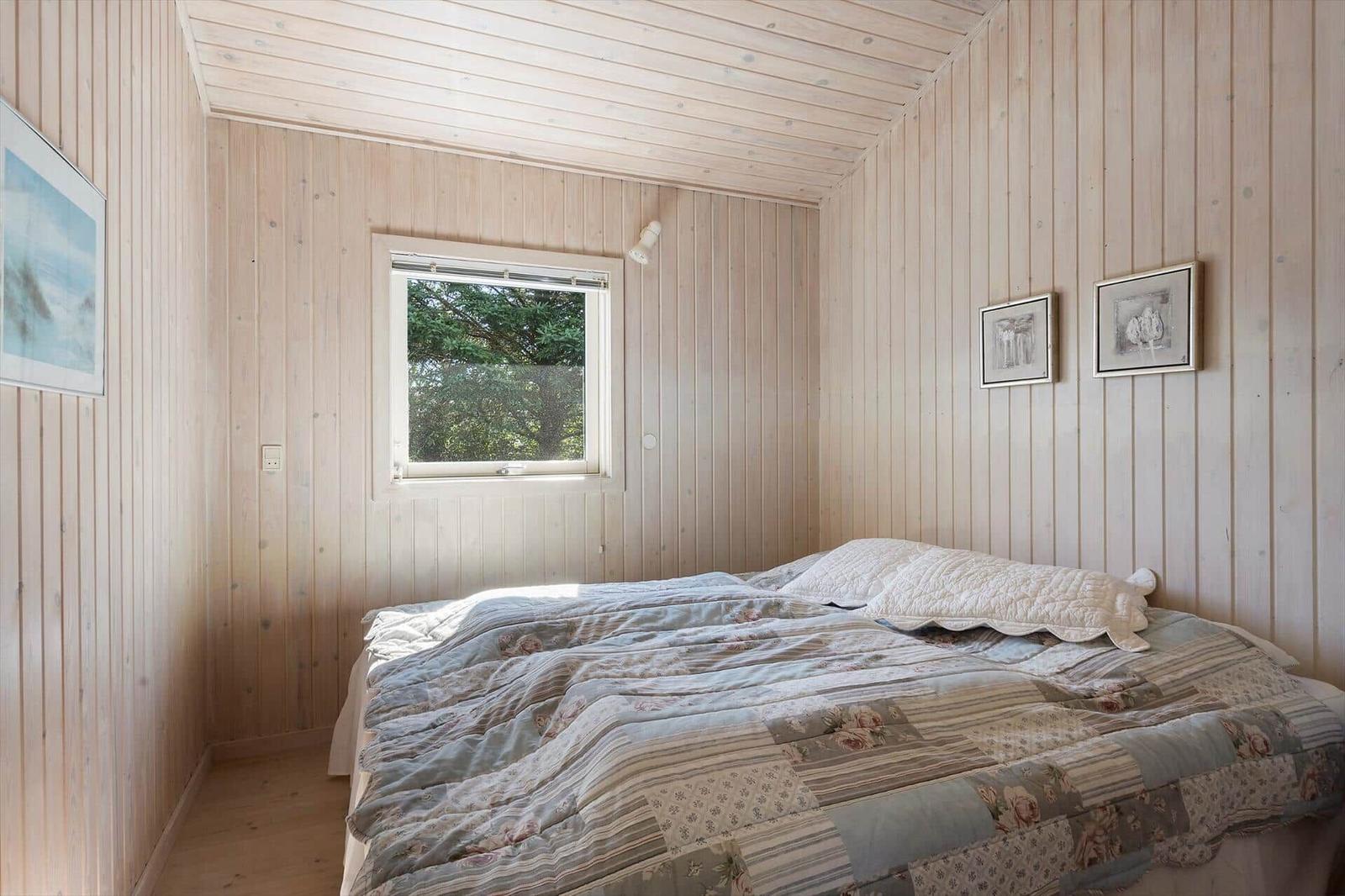 Schlafzimmer mit Holzwand, Bett und Fenster mit Blick auf Bäume.