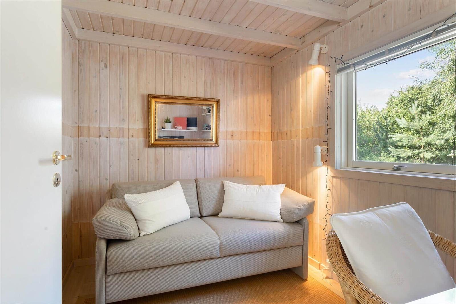 Ein Raum mit Holzwand, Sofa, Spiegel und Fenster mit Blick auf Bäume.