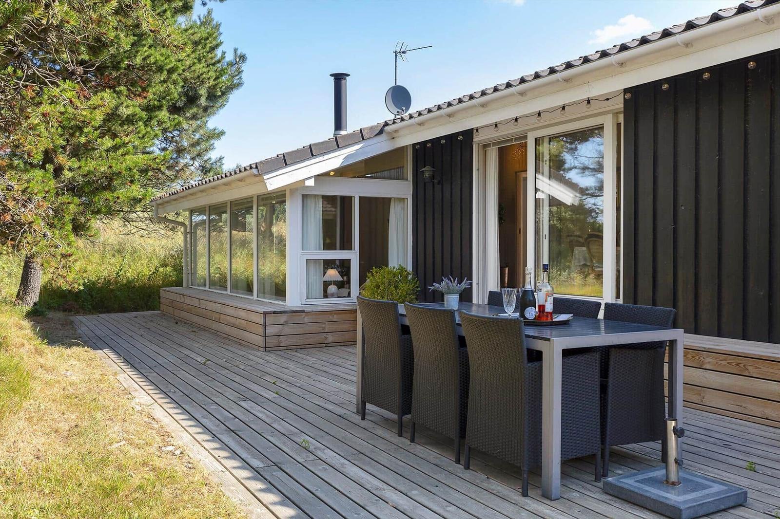Terrasse mit Tisch und Stühlen vor einem Haus mit großen Fenstern und Holzveranda.