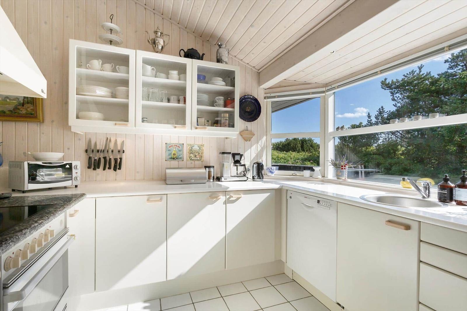 Küche mit weißen Schränken, Fensterblick auf Grün, Spüle und Küchengeräte.