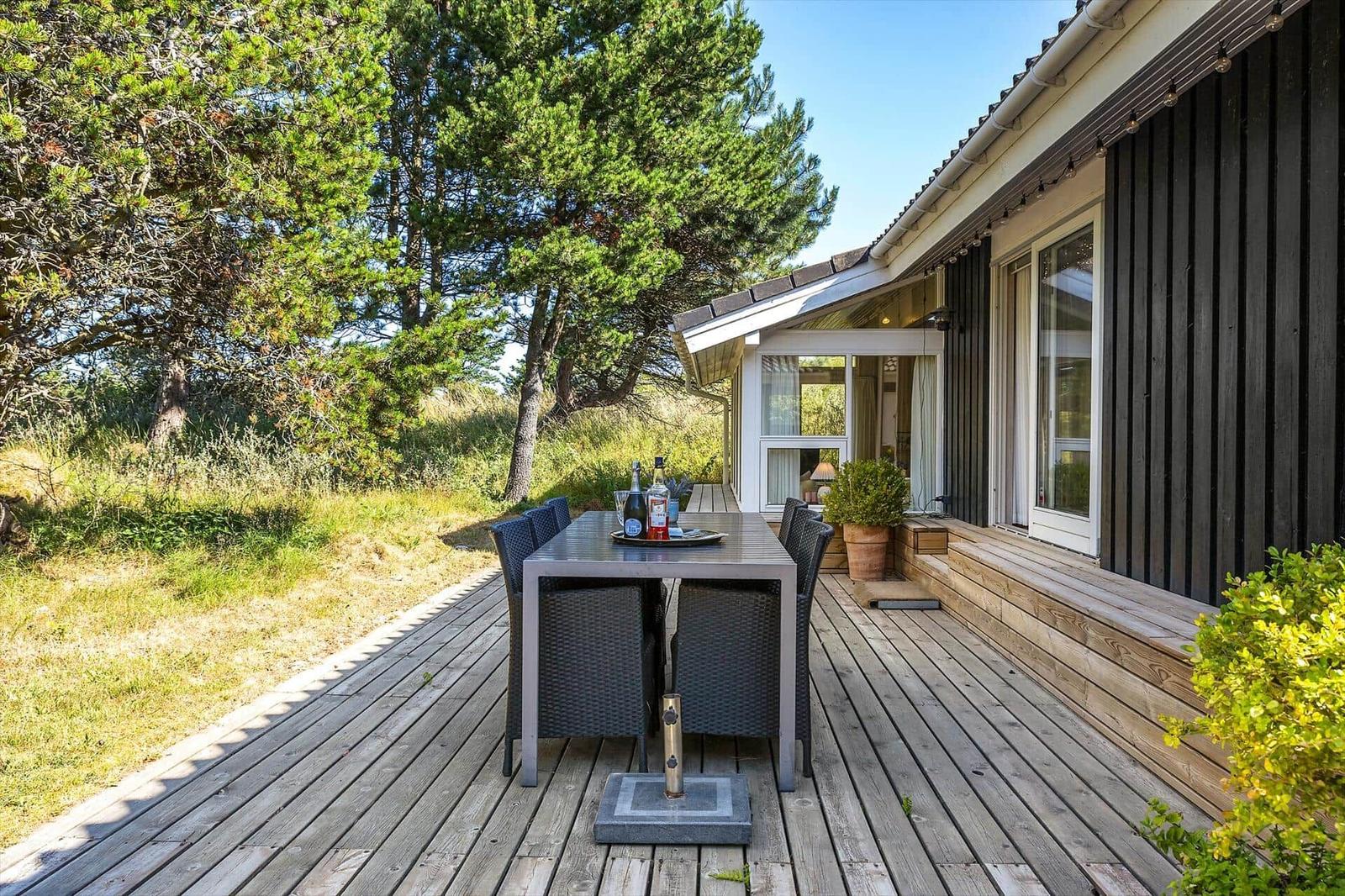 Terrasse mit Tisch und Stühlen neben einem Haus mit dunklem Holzverkleidung.