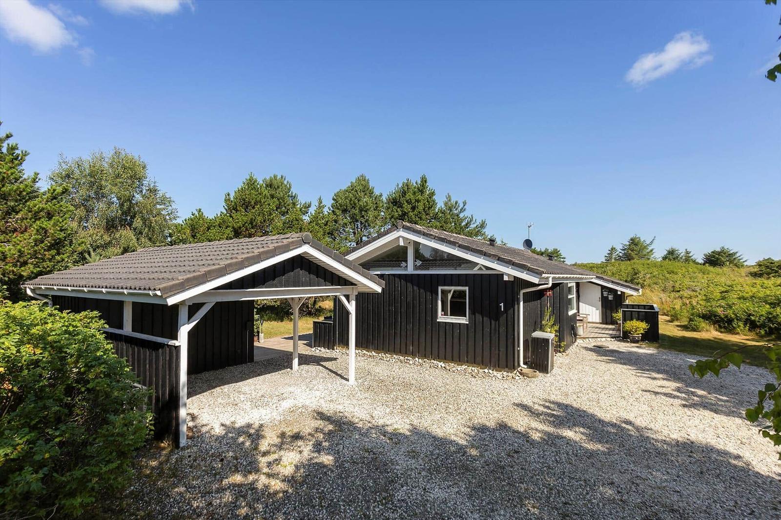 Schwarzes Holzhaus mit Carport und Kiesfläche, umgeben von Bäumen und Grün.