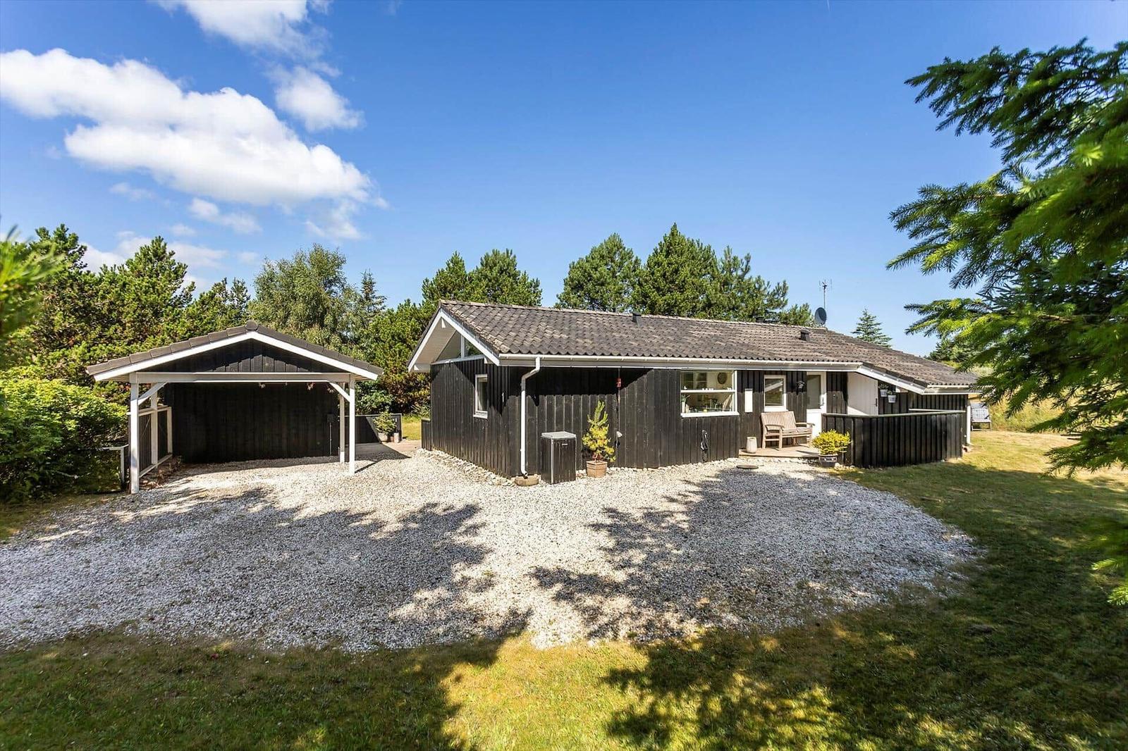 Ein Haus mit Carport, Kiesfläche und Grünanlagen umgeben von Bäumen.