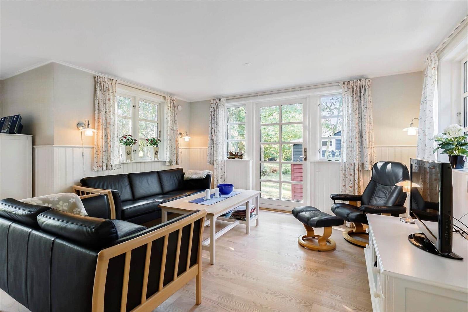 Living room with black leather furniture, wooden floor, and windows with curtains.