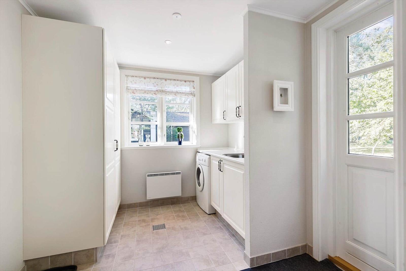 Laundry room with washing machine, windows, and white cabinets.