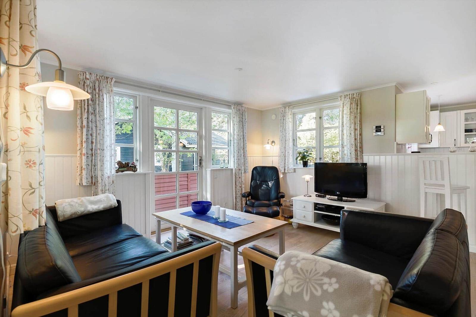 Living room with two black sofas, coffee table, and TV. Windows with curtains and wooden floor.