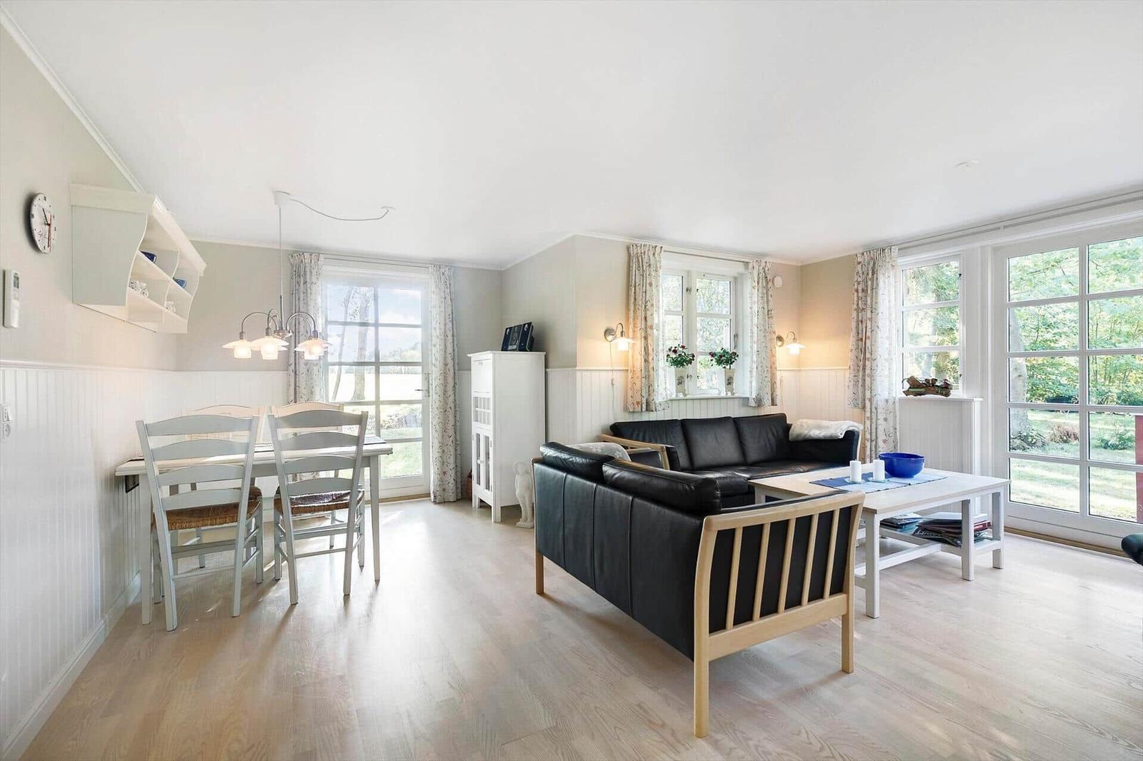 Living and dining area with sofa, table and chairs. Large windows with view of garden.