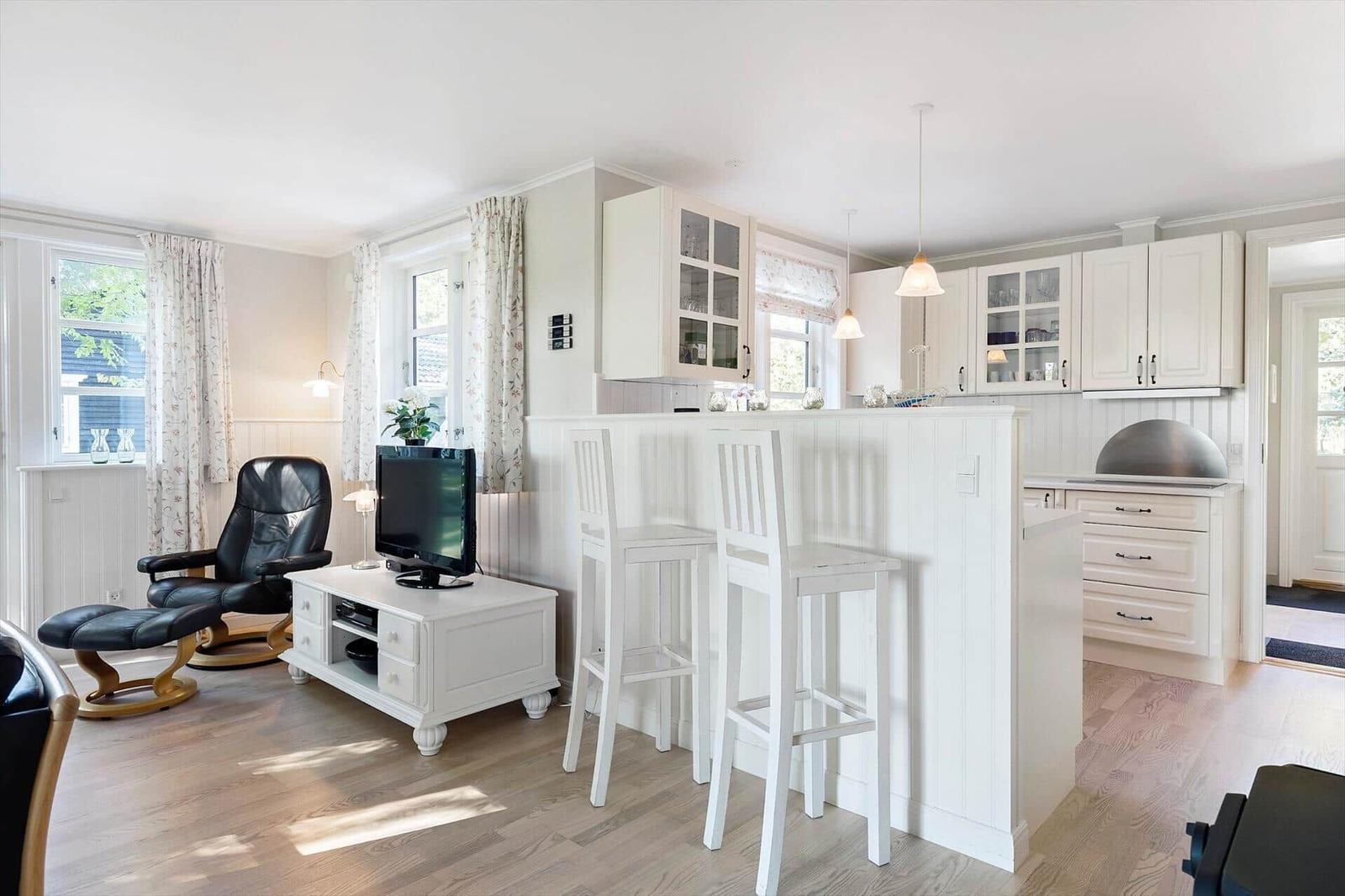 Living area with kitchen, black chair, and TV on white table.
