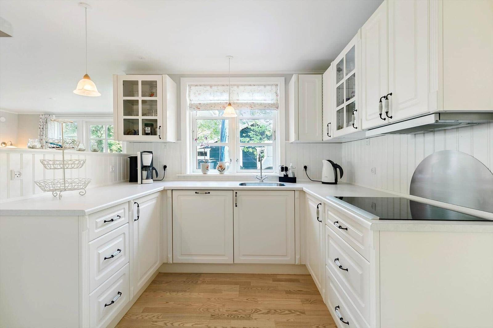 A white kitchen with wooden floor and window above the sink.