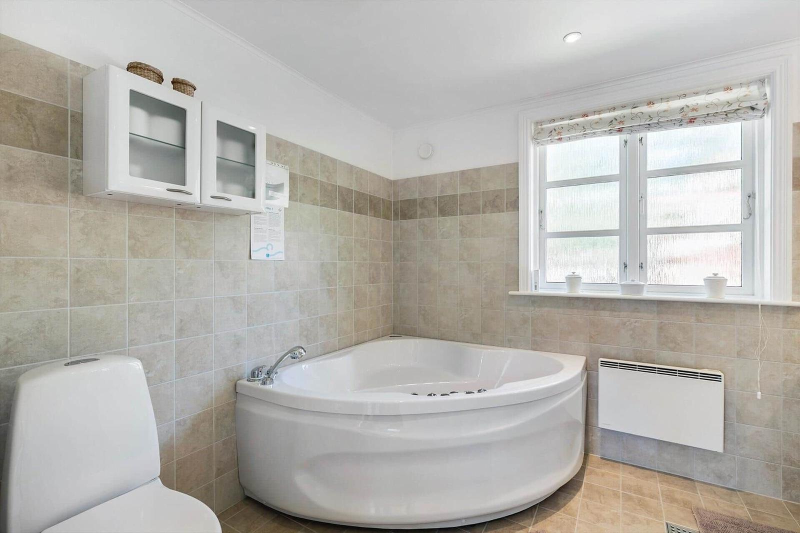 Bathroom with whirlpool, toilet, and window with roller blind.