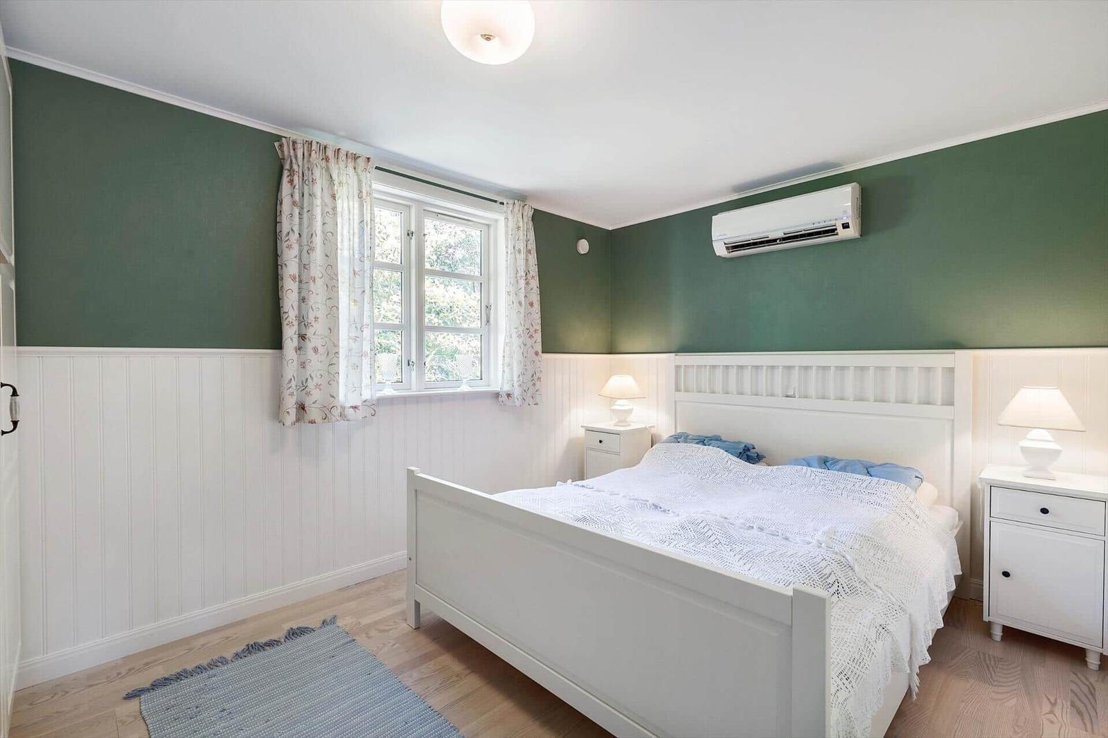 Bedroom with white bed, green walls and wooden floor. Window with curtains and nightstands.