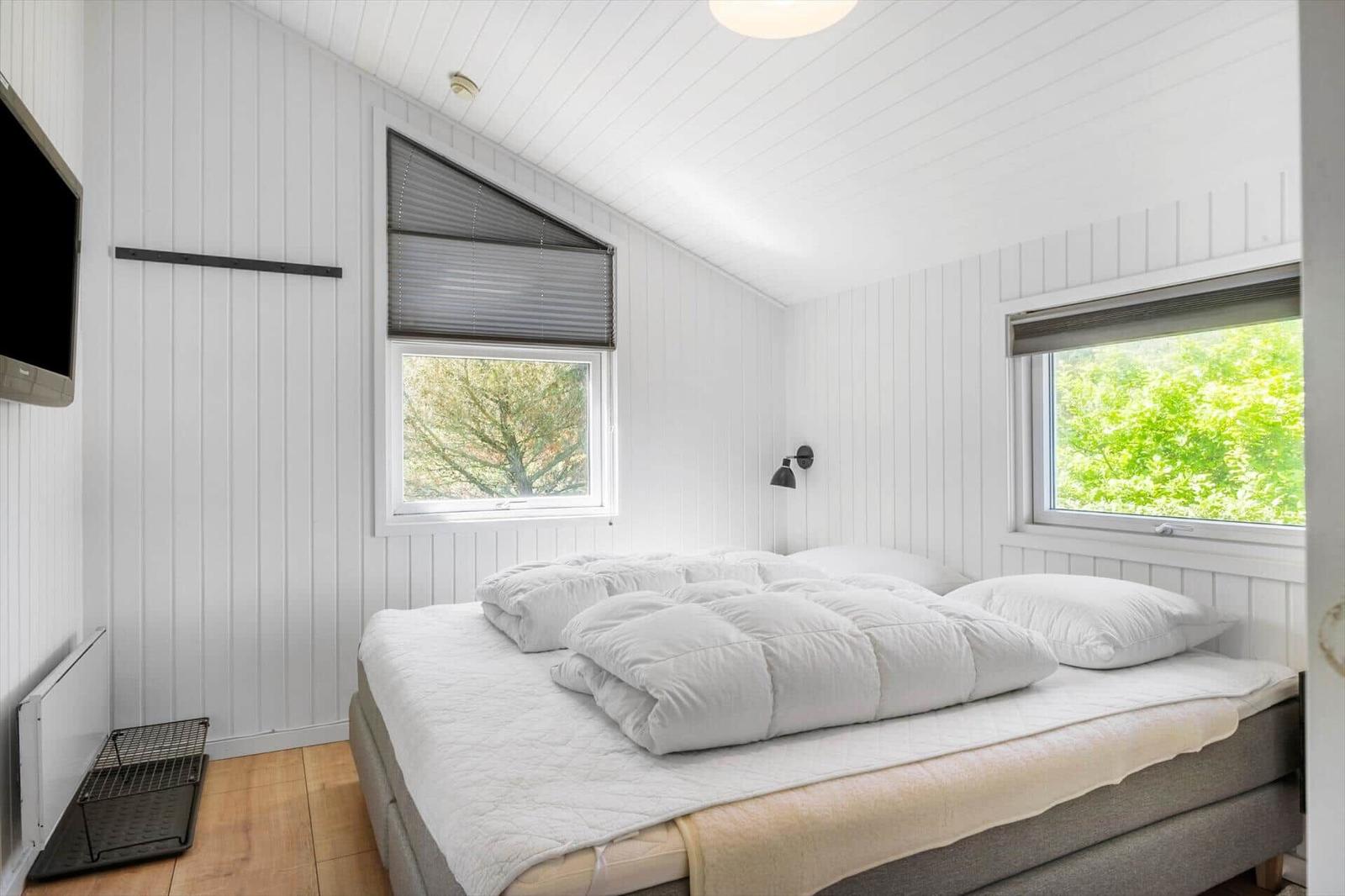 Schlafzimmer mit Bett, zwei Fenstern und Wand-TV.