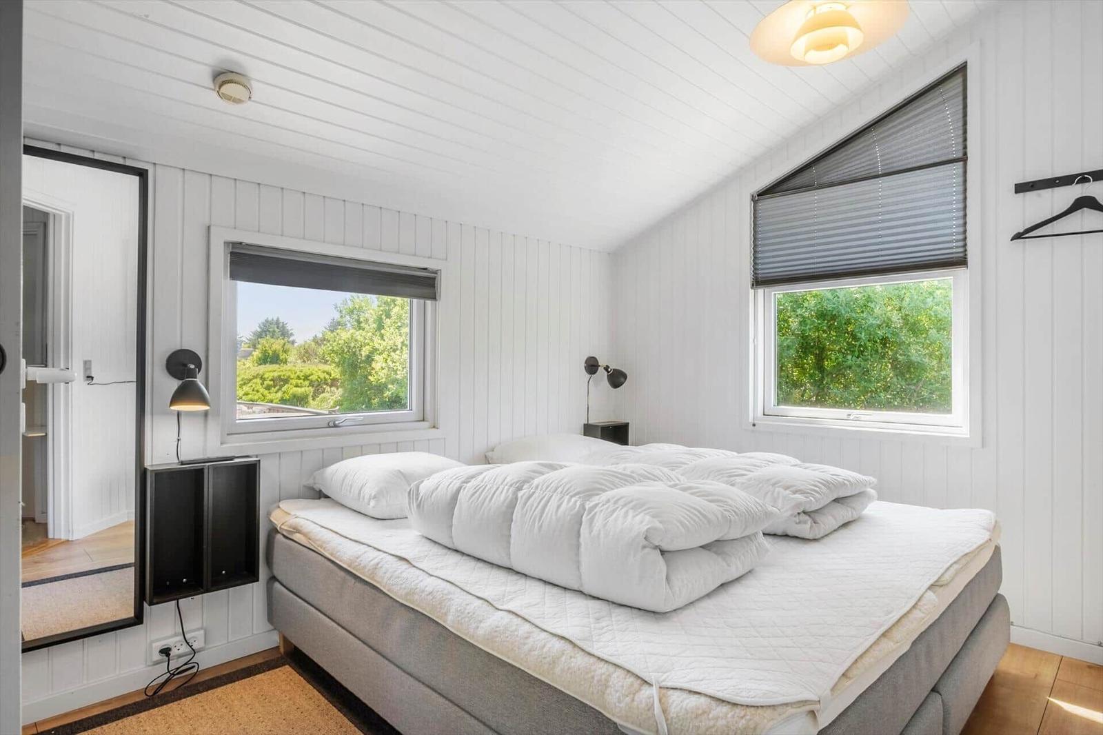 Schlafzimmer mit weißem Bett, Fenstern und Holzboden.