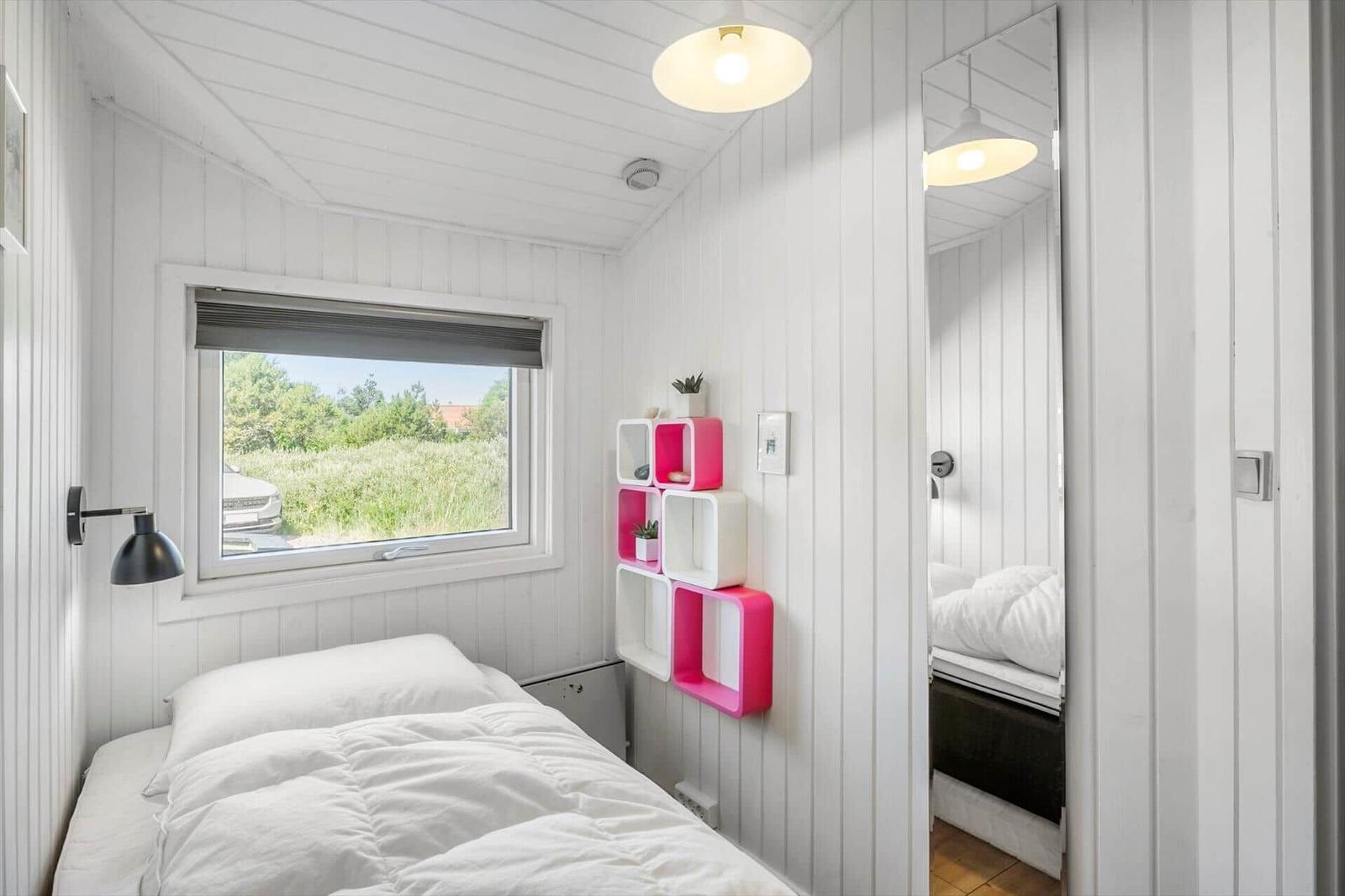 Schlafzimmer mit Bett, Fenster und Wandregal. Spiegel zeigt Bettreflexion.