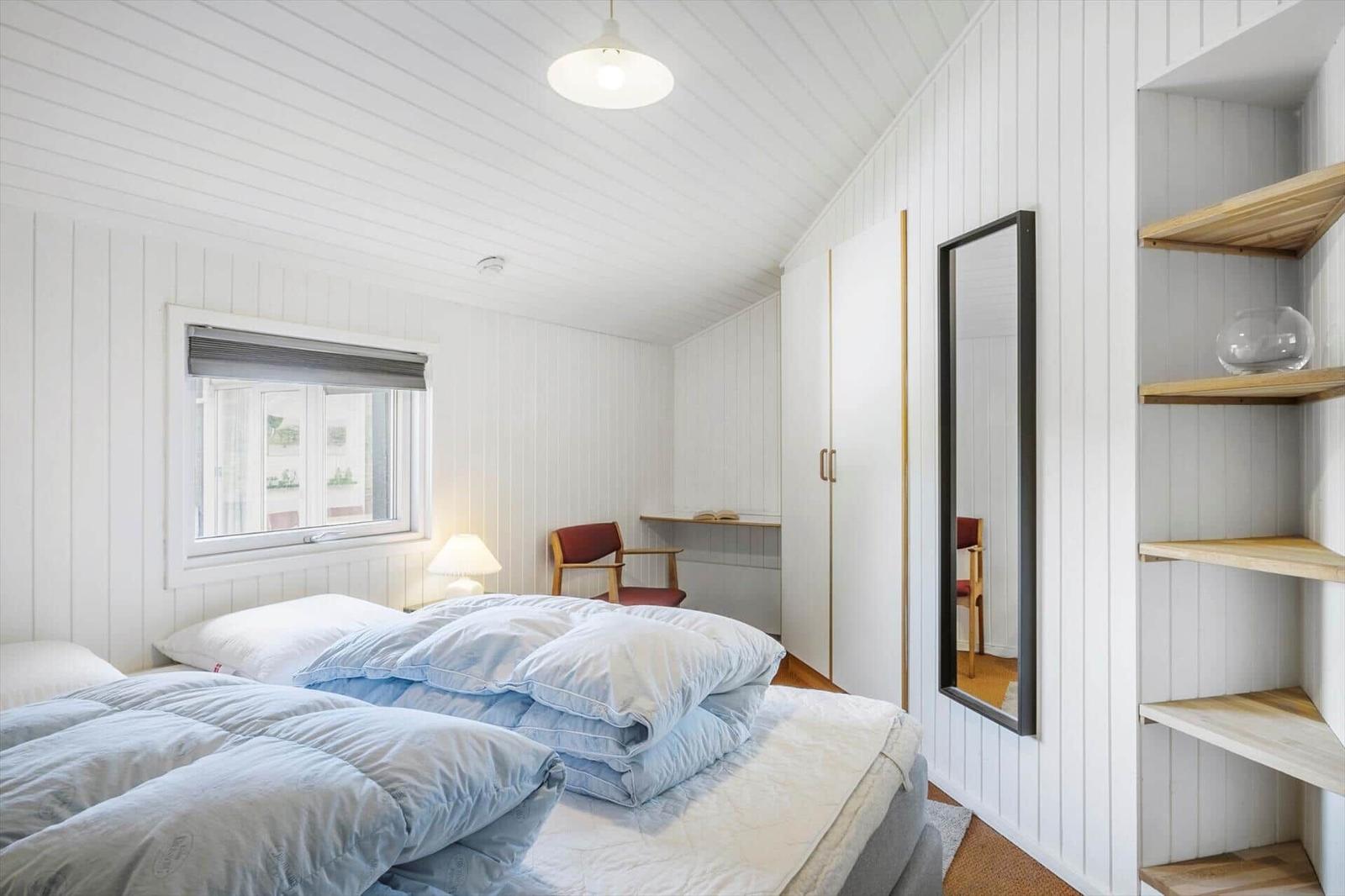 Schlafzimmer mit Bett, Fenster, Schreibtisch und Spiegel.