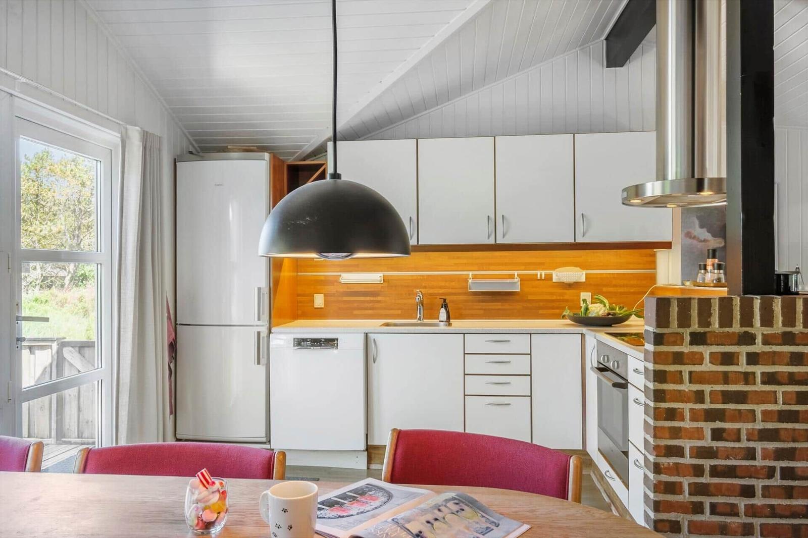 Küche mit weißen Schränken, Holzrückwand und Esstisch mit roten Stühlen.