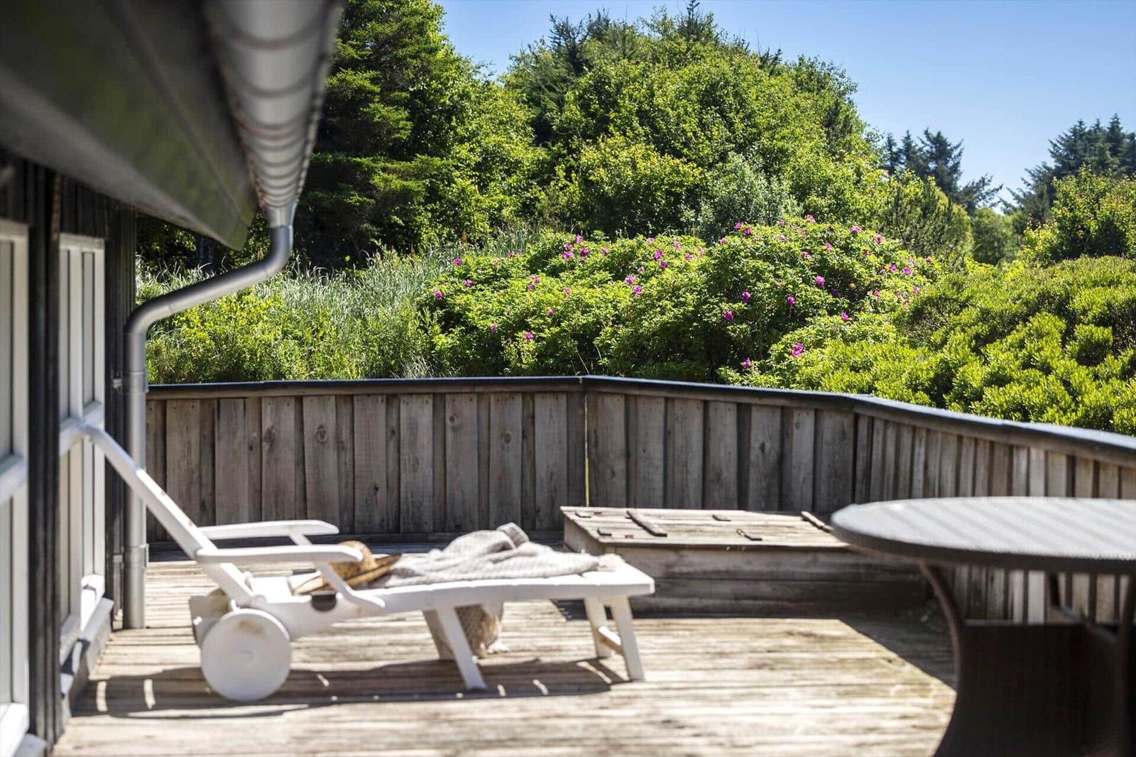 Terrasse mit Liegestuhl und Tisch, Blick auf grüne Bäume und Blumen.