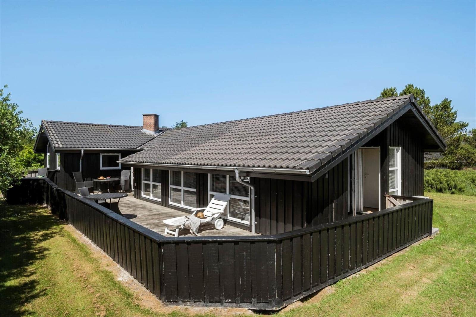Ein dunkel verputztes Ferienhaus mit Terrasse, Sonnenliege und Garten.