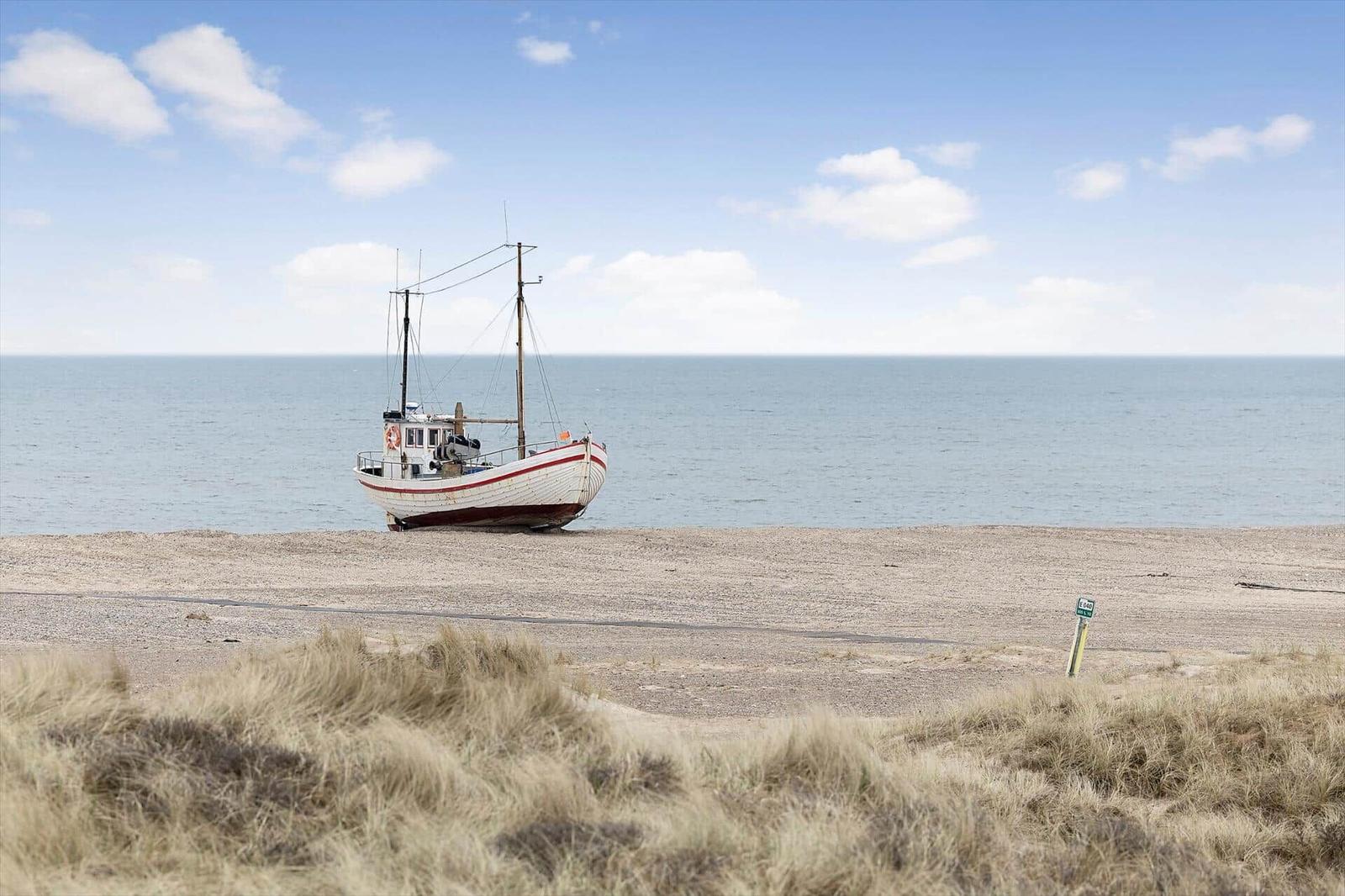 Ein weißes Fischerboot liegt auf einem sandigen Strand vor dem Meer.