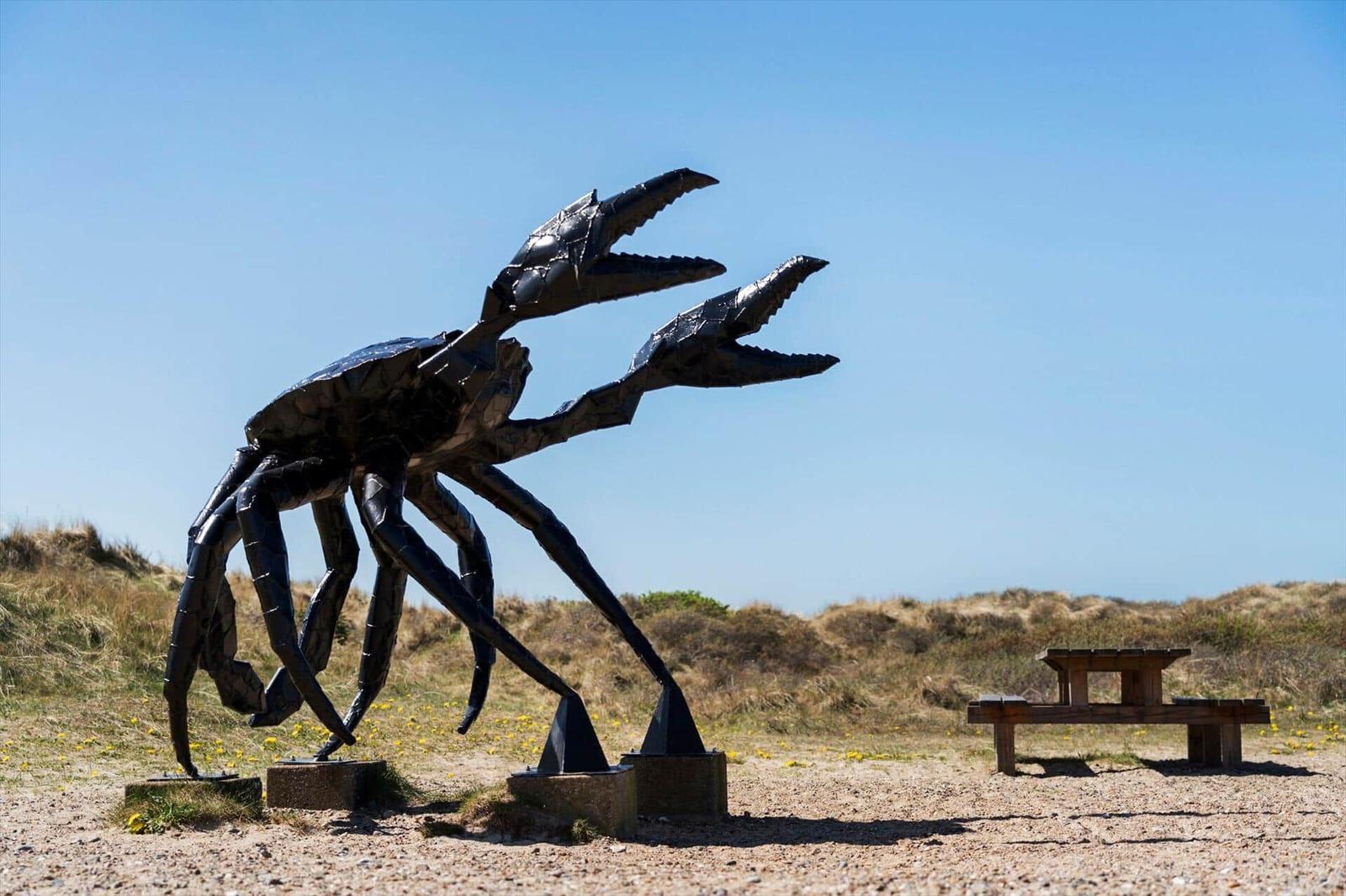 Große Krabbenstatue im Freien mit Picknicktisch auf sandigem Boden.