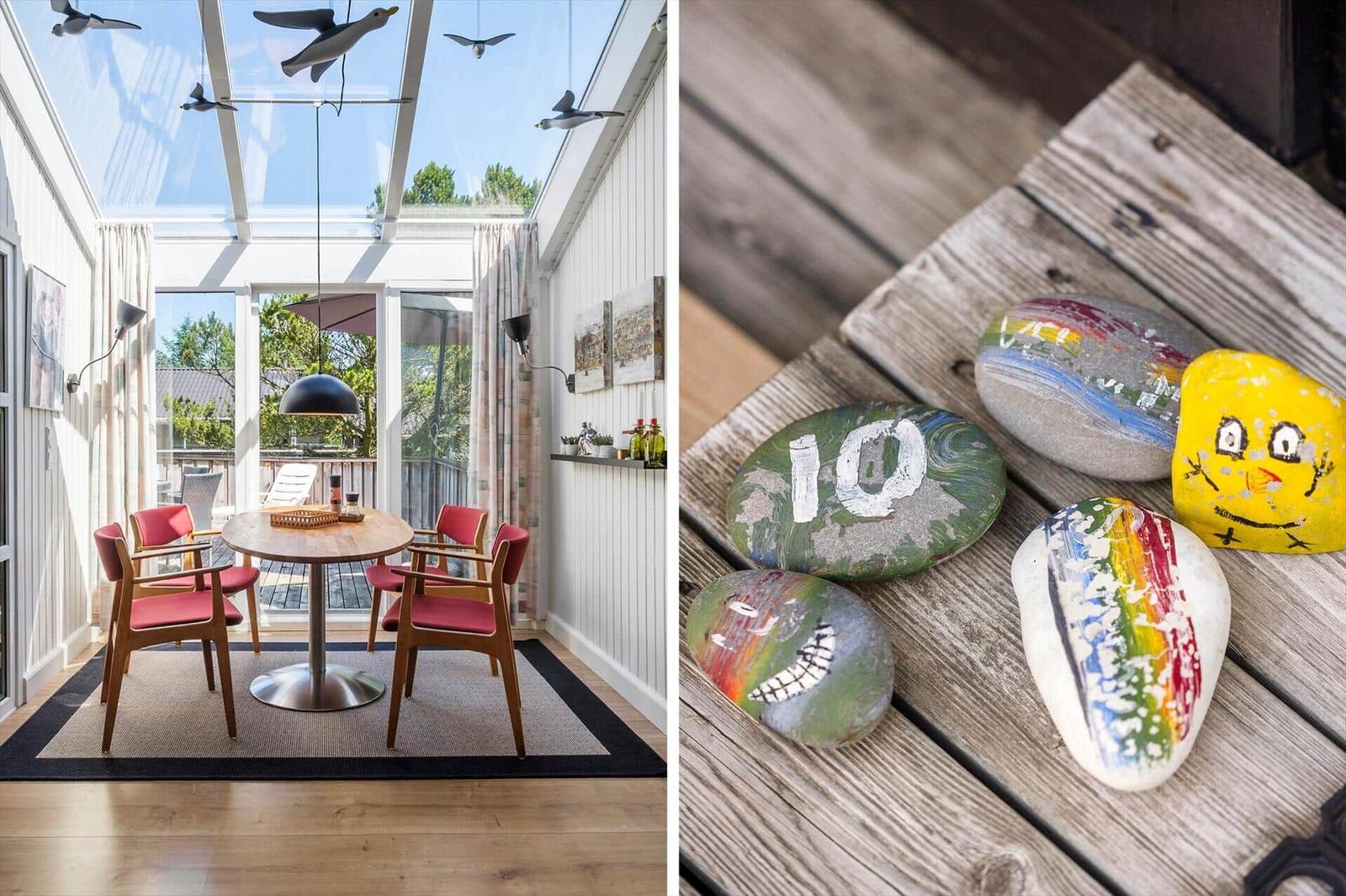 Terrassenbereich mit Tisch und Stühlen unter Glasdach. Farbig bemalte Steine auf Holzterrasse.