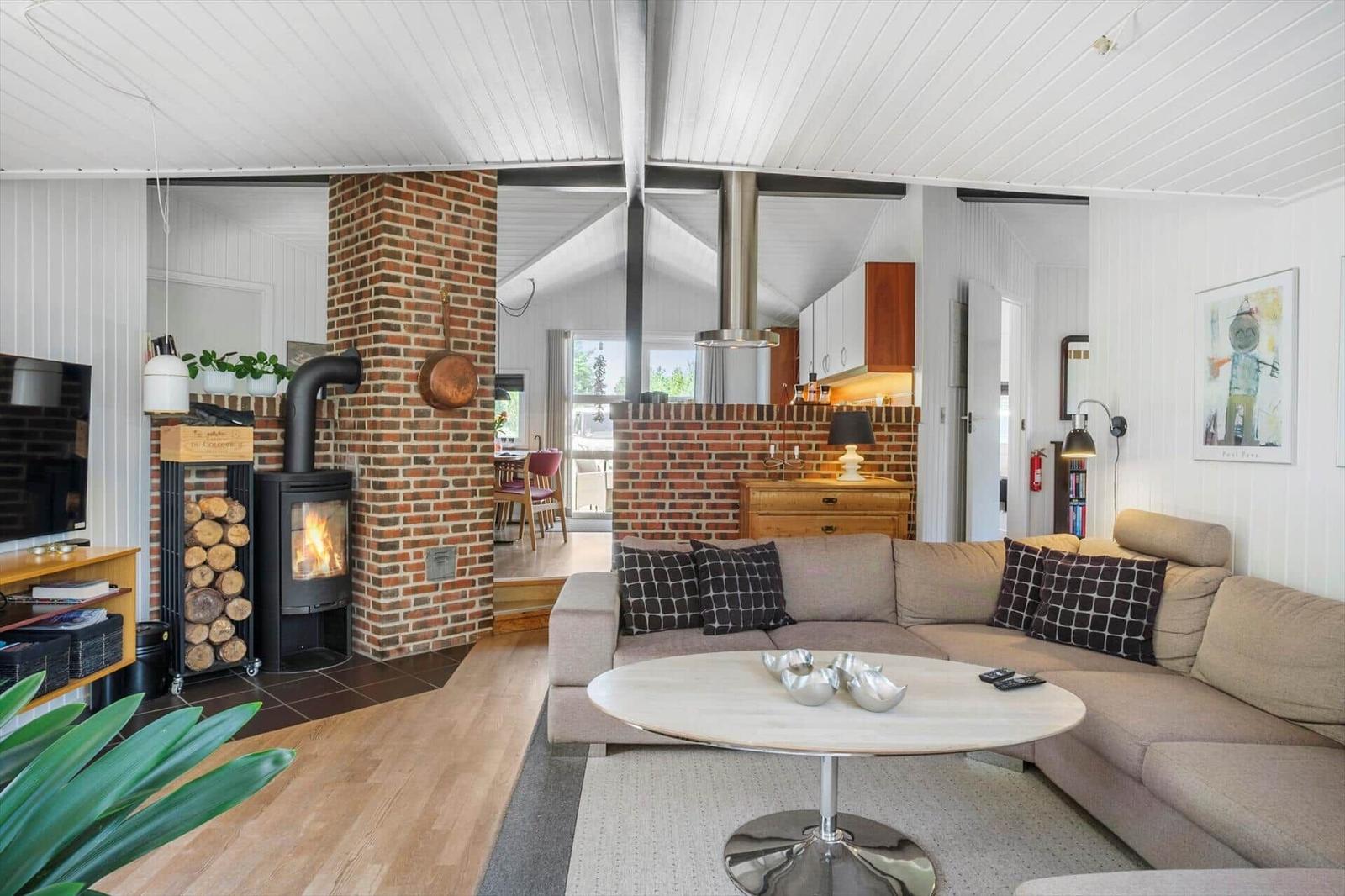 Wohnzimmer mit Sofa, Kamin und Holzboden. Küche im Hintergrund.