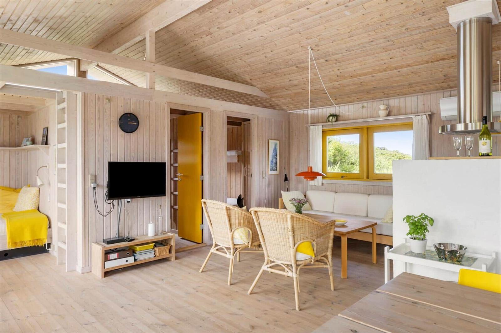 Wohnraum mit Essbereich, Sofa, Fernseher und Schlafzimmer mit gelber Bettwäsche.